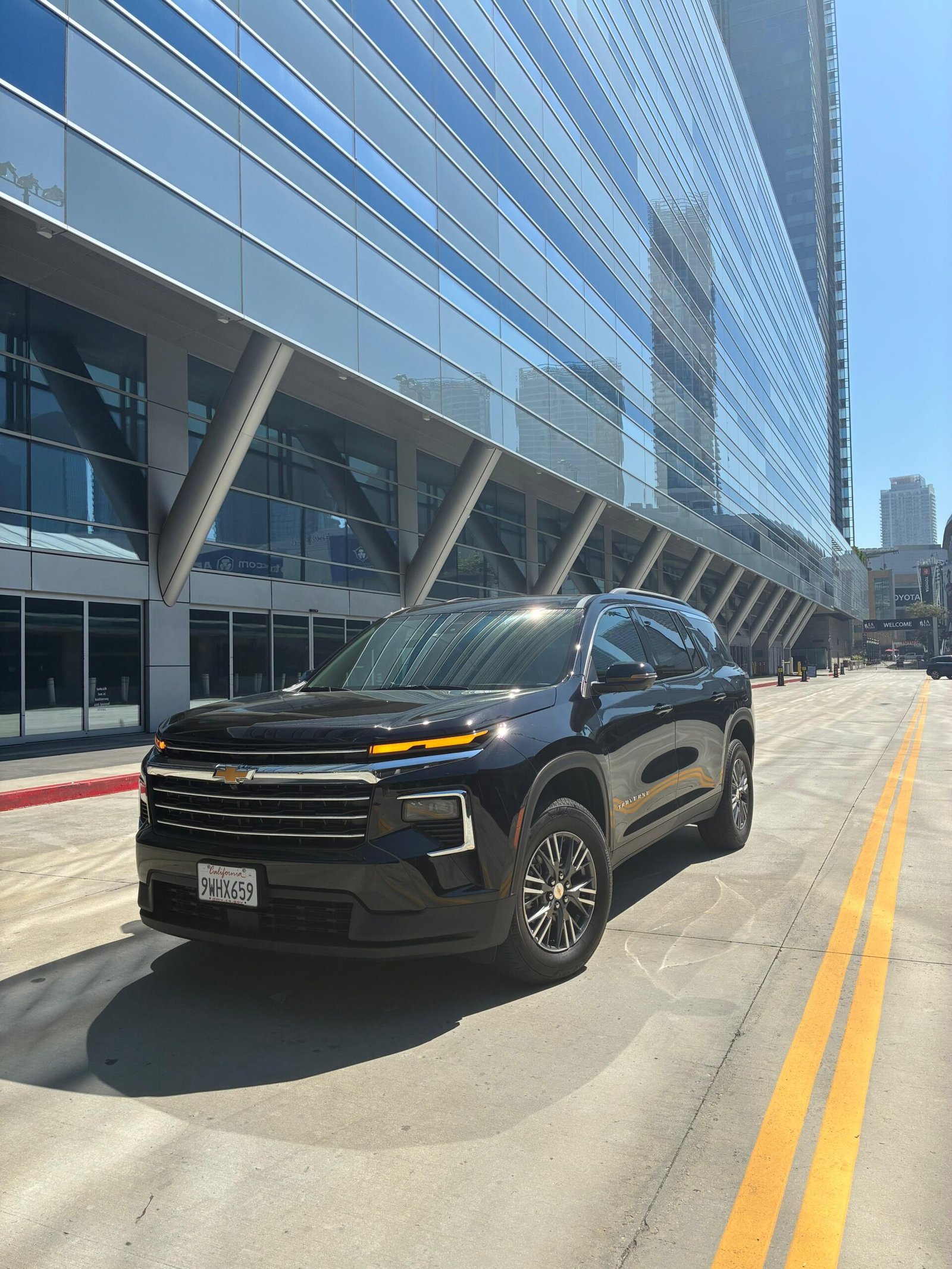 JM Transportation Service - Black 2026 Chevrolet Traverse SUV parked in front of modern glass building for luxury group transportation