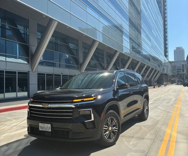 JM Transportation Service - Black 2026 Chevrolet Traverse SUV parked in front of modern glass building for luxury group transportation