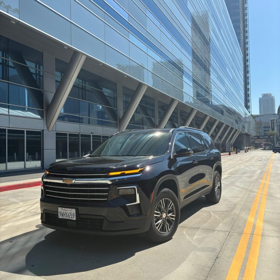 JM Transportation Service - Black 2026 Chevrolet Traverse SUV parked in front of modern glass building for luxury group transportation